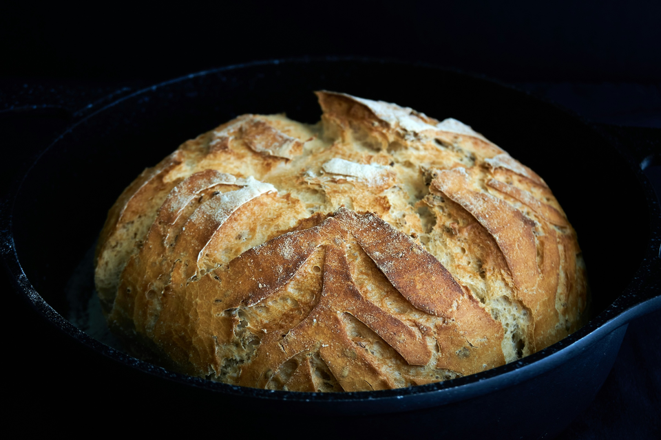 Fresh bread, in a rustic sourdough style, in a black cast iron pan.